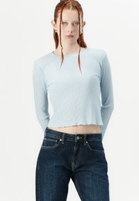 Light blue ribbed long-sleeve top with a cropped hem paired with dark denim jeans, featuring a smooth texture and subtle stretch.