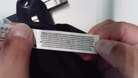 Mains tenant une étiquette de vêtement montrant la composition du tissu et les instructions d'entretien en plusieurs langues.