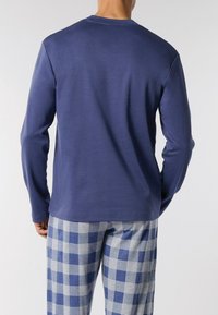 Camicia blu navy a maniche lunghe con scollatura rotonda, abbinata a pantaloni a quadri grigi e blu. Tessuto liscio, design casual.