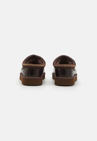 Brown leather slippers with a padded lining, brown rubber sole, and braided accent around the opening. Back view showing the rounded design.