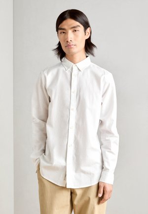 White button-up shirt made of cotton with a soft texture. Features a classic collar, long sleeves, and a subtle embroidered logo on the chest.