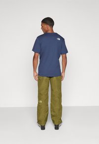 Navy blue short-sleeve t-shirt with a small white logo on the upper back, paired with light olive green cargo pants featuring subtle branding.