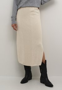 Jupe midi en tricot beige clair avec une texture côtel�ée, dotée de fentes latérales, associée à des bottes de cowboy noires.