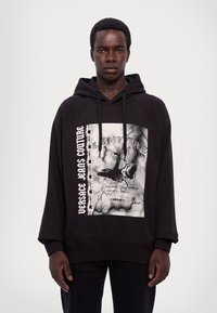 Felpa nera con cappuccio con una grafica frontale caratterizzata da un design invecchiato, testo bianco e motivo a catena, completata da un cordino e maniche raglan.