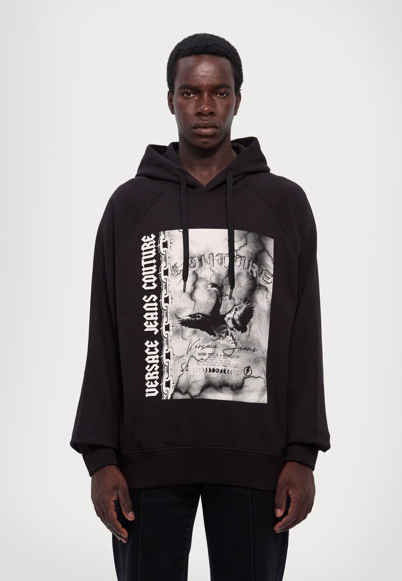 Felpa nera con cappuccio con una grafica frontale caratterizzata da un design invecchiato, testo bianco e motivo a catena, completata da un cordino e maniche raglan.