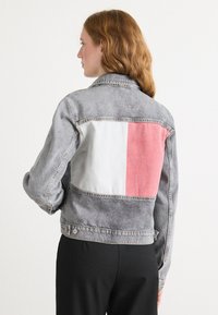 Jeansjack met een grijze body, gekenmerkt door een groot wit en roze blokontwerp op de rug. Klassieke kraag en knoopsluiting.