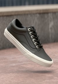 Zapatilla de piel negra con suela de goma blanca, puntera redondeada, seis ojales y un diseño texturizado en los laterales.
