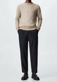 Beżowy dziany sweter z okrągłym dekoltem, zestawiony z dopasowanymi czarnymi spodniami i czarnymi botkami dla eleganckiego, nowoczesnego wyglądu.