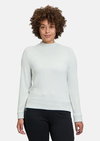 Ljusgrå, långärmad tröja med hög krage, ribbade muddar, mjukt material och en figursydd silhuett, matchad med svarta byxor.