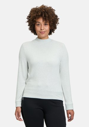 Helles graues, langärmliges Sweatshirt mit hohem Kragen, gerippten Manschetten, glatter Textur und taillierter Silhouette, kombiniert mit schwarzen Hosen.