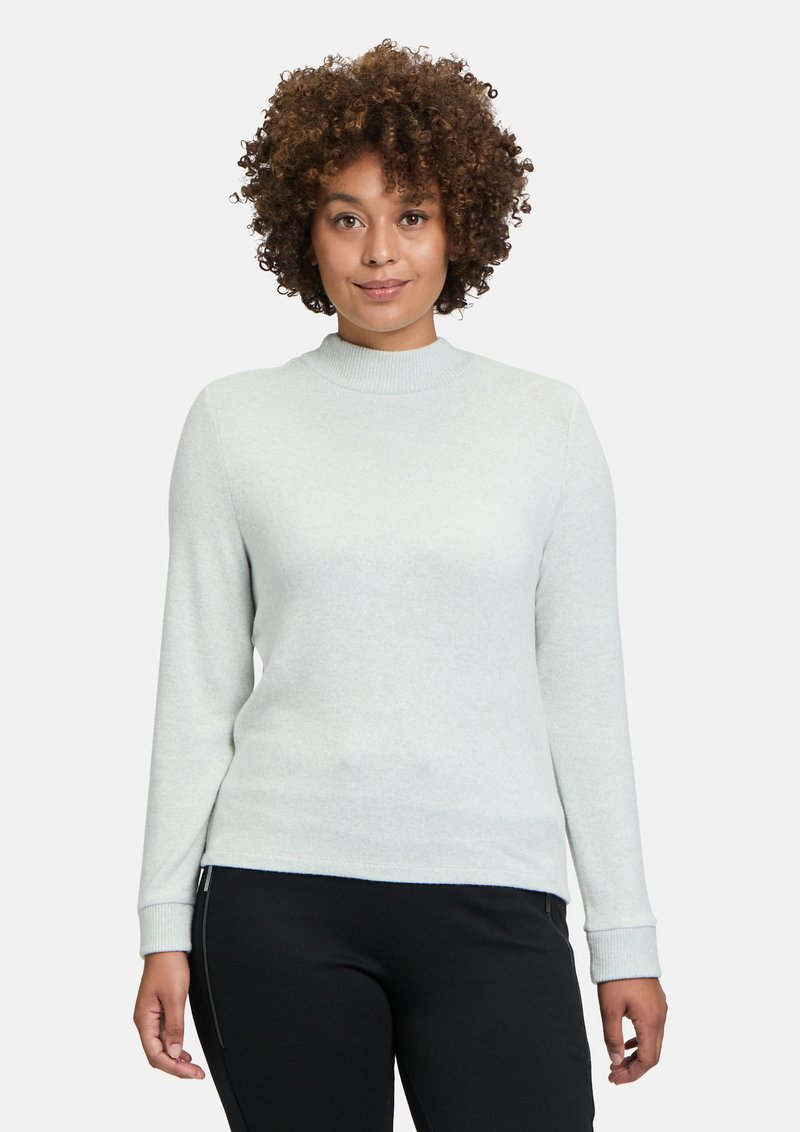 Ljusgrå, långärmad tröja med hög krage, ribbade muddar, mjukt material och en figursydd silhuett, matchad med svarta byxor.