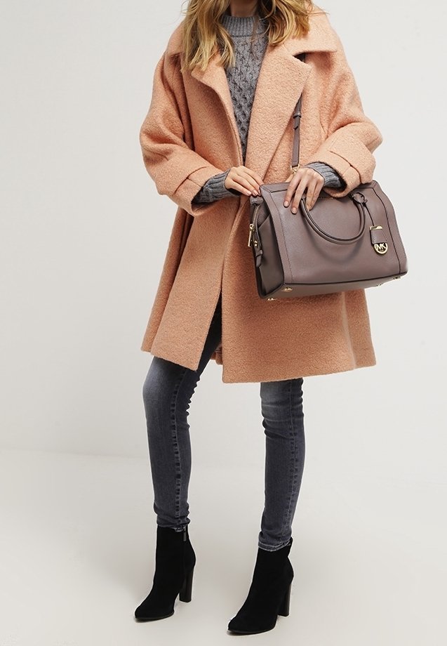 Femme portant un manteau en laine pêche, un pull gris, un jean skinny foncé, des bottines noires à talons, et tenant un grand sac à main marron.