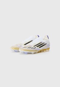 Scarpe da calcio bianche con accenti dorati e viola, dotate di una tomaia testurizzata, tre strisce nere e una suola traslucida con tacchetti.