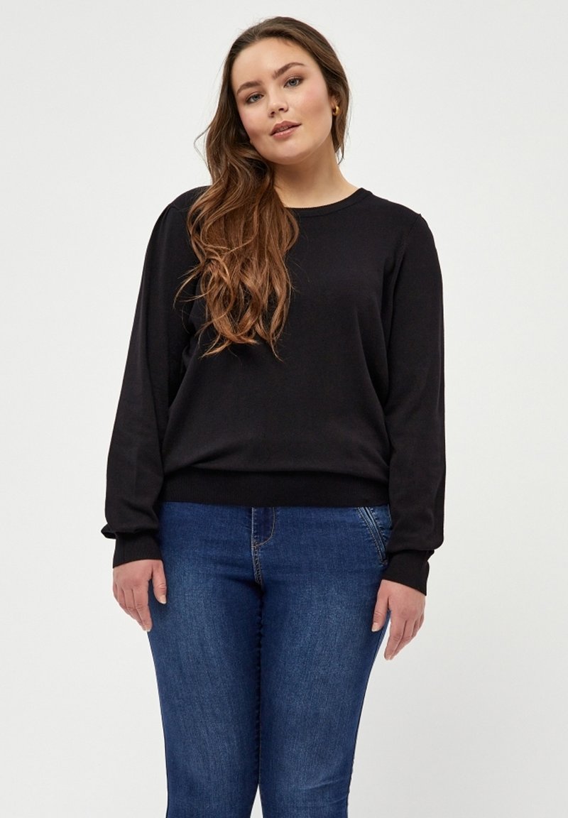 Sort, langærmet trøje med rund hals, lavet af blødt materiale. Sammen med blå denim jeans. Enkel design med tætsiddende manchetter.