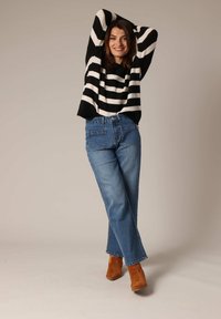 Pull oversized à rayures noir et blanc en tissu doux, associé à un jean en denim bleu taille haute et des bottines en daim marron.