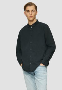 Camisa negra de botones con cuello, mangas largas y ajuste ceñido; combinada con jeans de mezclilla azul claro; textura suave y diseño sencillo.