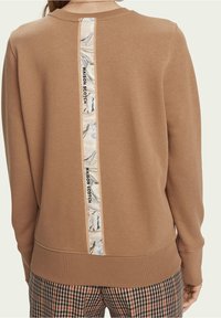 Bruine sweater met een verticale gemarmerde stoffen strook en logo details op het midden van de achterkant. Zacht textuur en geribbelde manchetten.