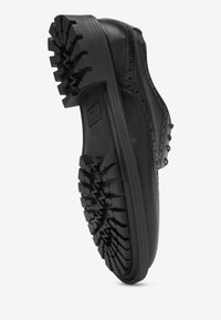 Scarpa di pelle nera con tomaia liscia, dettagli brogue e una suola in gomma spessa e robusta con scolpiture profonde per una migliore aderenza.