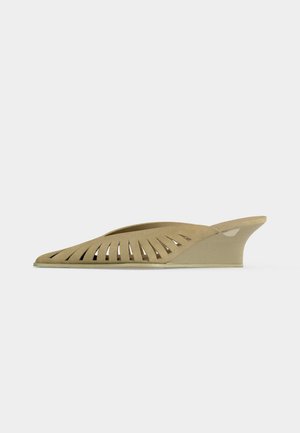 Beige sleehak mule met uitgesneden design langs de zijkant, met een puntige neus en lage hak.