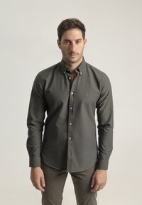Camisa abotonada verde oscuro hecha de una tela suave, con un collar, mangas largas y botones blancos. Ajuste slim con un dobladillo curvado.