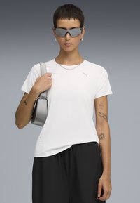 Hvid kortærmet T-shirt med rund hals, der har et lille logo, kombineret med sorte bukser og en metallic sølv håndtaske.