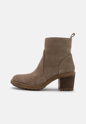 Bottine en daim taupe avec petit talon bloc, bout arrondi, languette à l'arrière, et coutures décoratives le long des côtés et de la semelle.