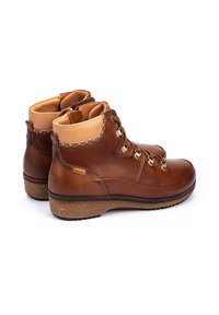 Bottines en cuir marron avec une finition lisse, col en tan contrastant, œillets en métal et talon texturé. Semelle en liège pour une meilleure adhérence.