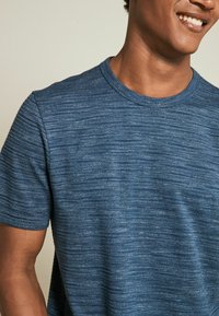 Tricou scurt cu mânecă scurtă, de culoare albastră, cu un model texturat cu dungi orizontale și un guler clasic de tip crew neck, realizat dintr-un material moale și ușor.