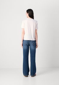 T-shirt bianco a maniche corte abbinato a jeans in denim blu scuro a gamba svasata. La t-shirt ha un taglio dritto; i jeans presentano uno stile classico a cinque tasche.
