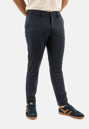 Men's dark navy chinos with a slim fit, made of soft fabric, featuring front pockets and a flat front design paired with dark sneakers.