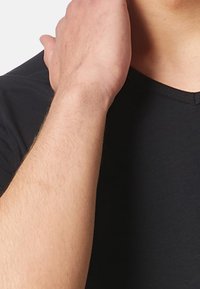 T-shirt noir à col en V, fabriqué en tissu lisse, présentant un gros plan d'un bras à la peau claire reposant sur l'épaule, mettant en valeur l'encolure.