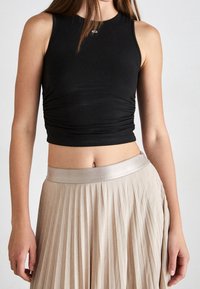Top croppato nero aderente con scollatura rotonda e leggera arricciatura, abbinato a una gonna beige plissettata con una cintura in satin lucido.