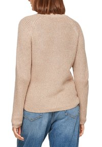 Beige gebreide trui met een gemêleerde afwerking, lange mouwen en een ronde halslijn, gecombineerd met blauwe spijkerbroeken.