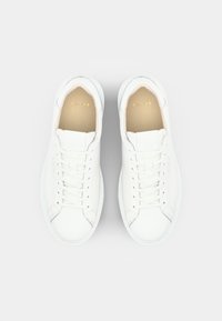 White leather sneakers with a smooth texture, rounded toe, lace-up front, and subtle branding in gold on the insole.