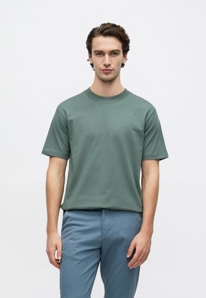 Camiseta de algodón verde con mangas cortas, cuello redondo y un ajuste relajado, combinada con pantalones azul claro. Diseño sencillo, sin estampados.