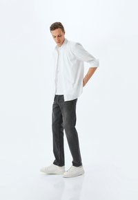 Camisa blanca de algodón con botones, jeans de mezclilla gris y zapatillas blancas. La camisa tiene las mangas dobladas y un corte relajado.