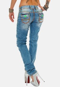 Jeans in denim blu snodati presentano cuciture decorative, due tasche posteriori con accenti verdi e una vita a media altezza.