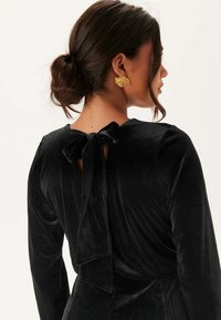 Robe en velours noir avec manches longues et détail de lien au dos. Texture lisse avec une coupe élégante pour mettre en valeur la silhouette.