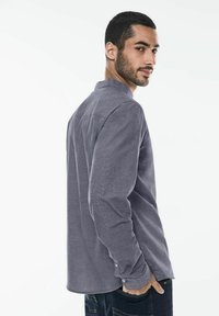 Camicia a maniche lunghe con colletto in tessuto grigio scuro con una trama strutturata. Presenta dettagli con bottoni sui polsini e una vestibilità comoda.