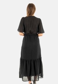 Vestido maxi a rayas negras con mangas cortas, cintura ceñida y parte inferior con volantes y acampanada. Hecho de una tela ligera y transparente.