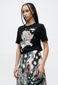 Zwart katoenen T-shirt met een meerkleurige afbeelding van een tijger en diverse hemelse elementen. Gecombineerd met een rok versierd met sterren.