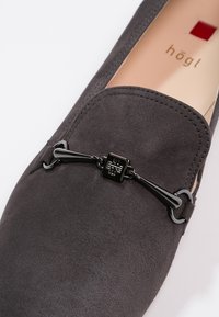 Mocassin en daim gris foncé avec détail en métal noir et semelle intérieure beige estampillée « högl », photographié sur fond blanc.