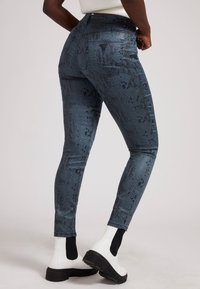 Jeans ajustados en un estampado de serpiente azul oscuro, con una cintura alta, bolsillos traseros y una textura suave y ligeramente brillante. Combinados con botas blancas de tobillo.
