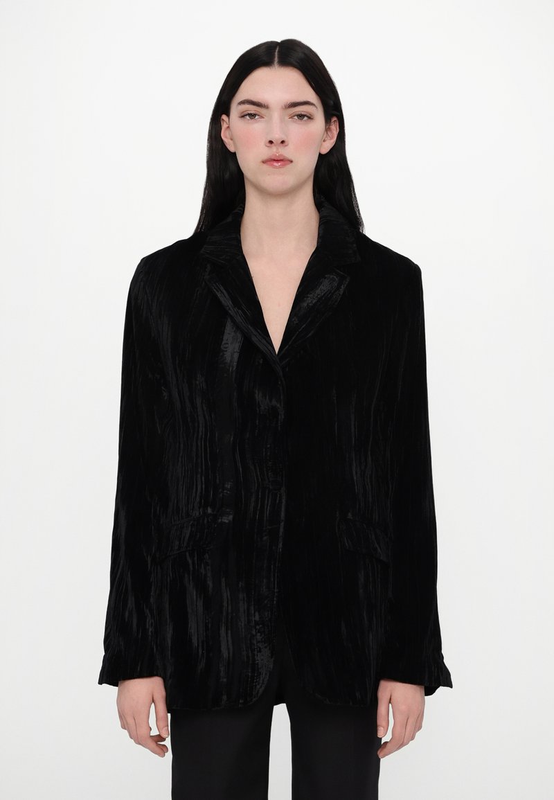 Schwarze Samtjacke mit Revers, zwei Fronttaschen und einer strukturierten Oberfläche. Das Design ist tailliert und hat eine leicht lockere Passform.
