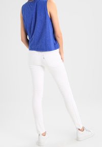 Top sin mangas azul hecho de una tela suave, combinado con jeans blancos ajustados y zapatillas blancas. El conjunto presenta un diseño simple y limpio.