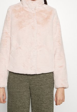 Veste en fausse fourrure rose clair avec col montant portée sur un pantalon tricoté vert olive, vue des épaules jusqu'aux hanches.