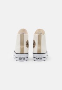 Wysokie trampki z kremowej skóry z złotymi akcentami, wyposażone w okrągłą naszywkę z logo, białą podeszwę i czarny pasek na podeszwie.