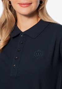 Námořnický polo tričko vyrobené z texturované tkaniny, s límečkem, pěti černými knoflíky a diskrétním vyšitým logem s korunou a vavřínem.