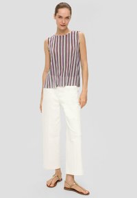 Mouwloze gestreepte blouse in wit, paars en rood. Gecombineerd met wijduitlopende witte jeans en bruine platte sandalen. Minimalistisch ontwerp en snit.