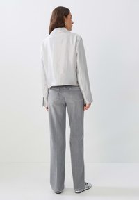 Silberner, metallischer Kurzjacke mit Kragen, kombiniert mit hellgrauen, geraden Jeans. Glatte Textur und minimale Details.